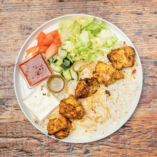 A plate of grilled chicken, rice, fresh salad, and various sauces on a wooden table.