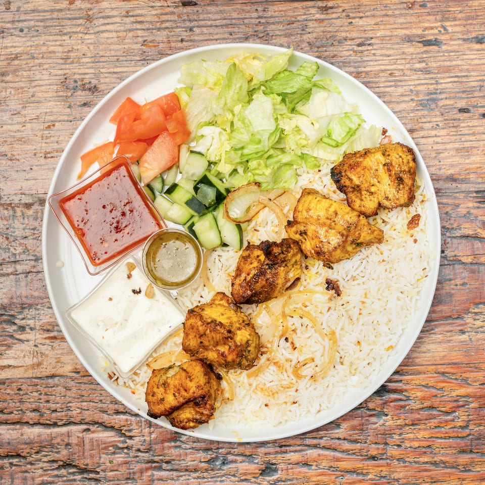 A plate of grilled chicken, rice, fresh salad, and various sauces on a wooden table.