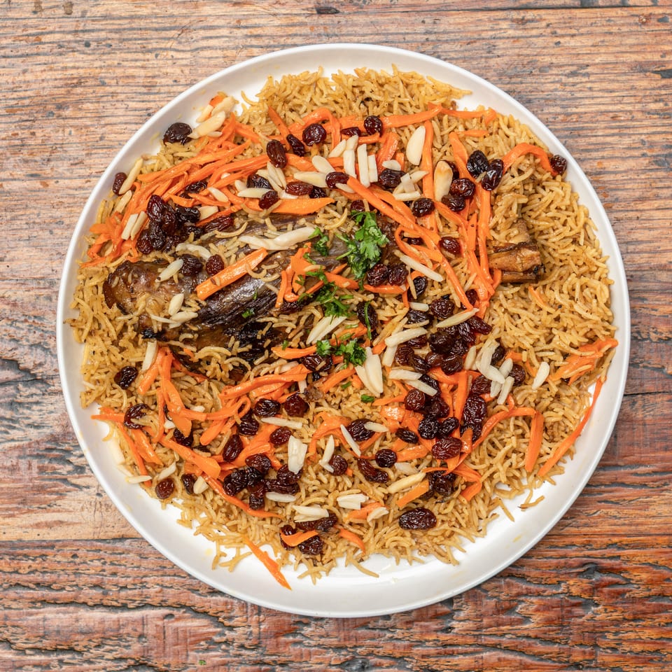 Savory rice dish with meat, julienned carrots, dark raisins, and sliced almonds on a white plate.