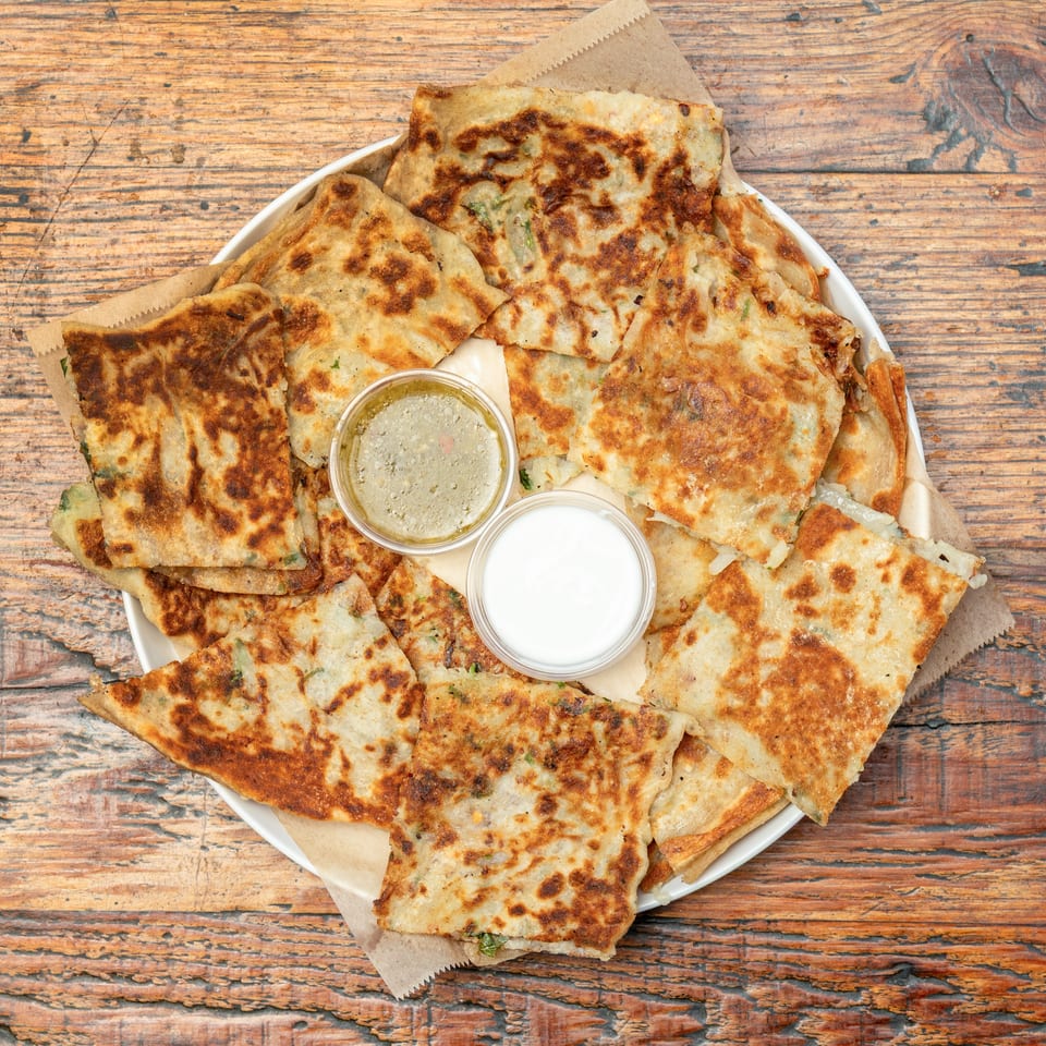 Savory golden-brown flatbreads with herbs, served with white and green dipping sauces on a wooden table.