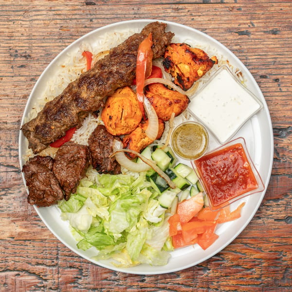 Mixed grill platter with kebab, chicken tikka, beef, rice, salad, and various sauces.