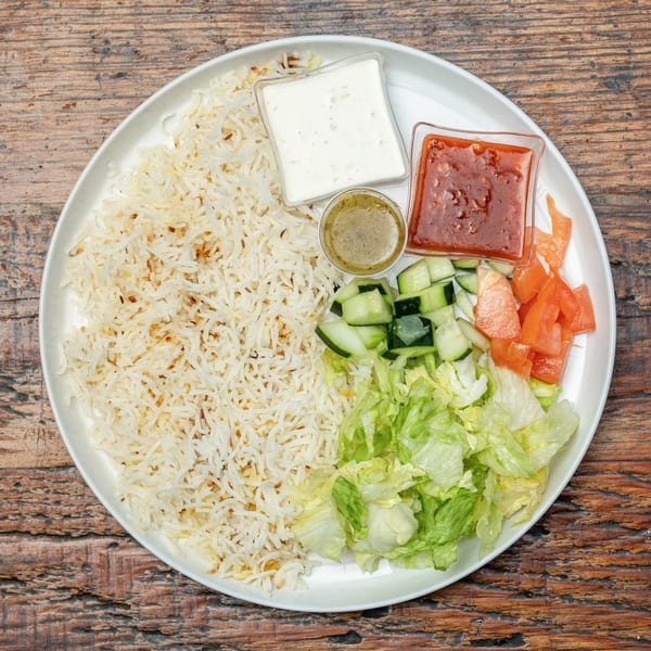 White plate with rice, chopped lettuce, cucumber, tomato, and three dipping sauces on a wooden table.