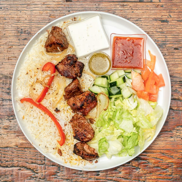 Grilled meat skewers, rice, sautéed vegetables, fresh salad, and three sauces on a white plate.