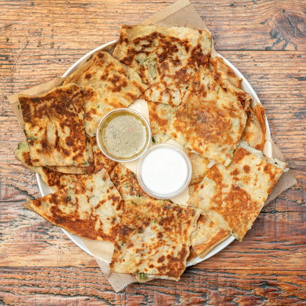 Golden-brown savory flatbread squares with herbs and two dipping sauces on a wooden table.